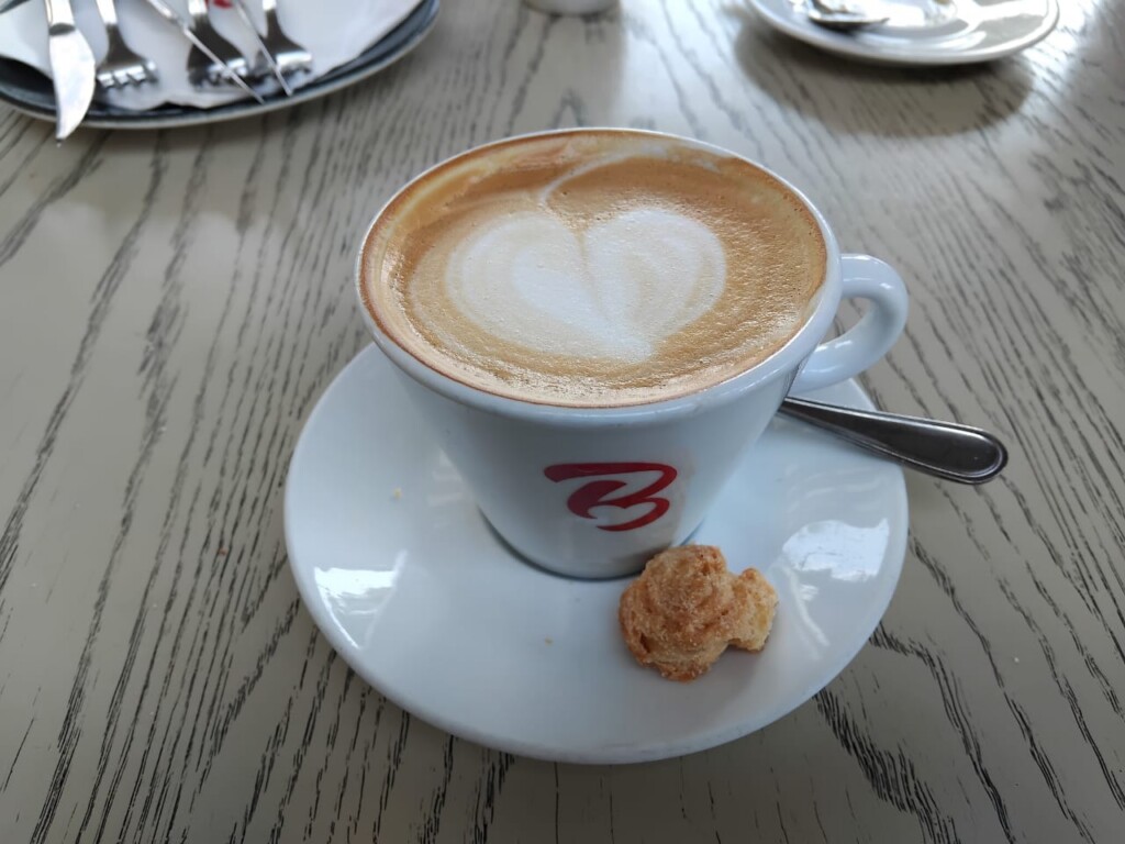 Freshly prepared cappuccino with heart-shaped milk foam served in a Bem Bom coffee cup.