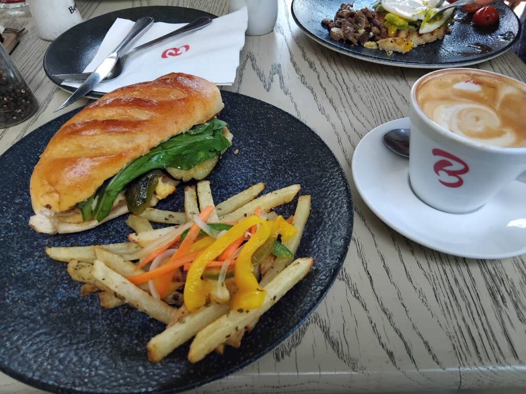 Mediterranean-style sandwich with chips and pickled vegetables served with a cappuccino at Bem Bom Café.