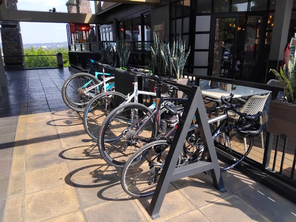 Road bicycles parked in a dedicated outdoor bicycle rack beside the Bem Bom Café terrace.